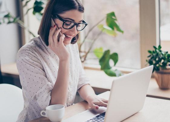 Woman talking on the phone and reading about freelance taxes on her laptop