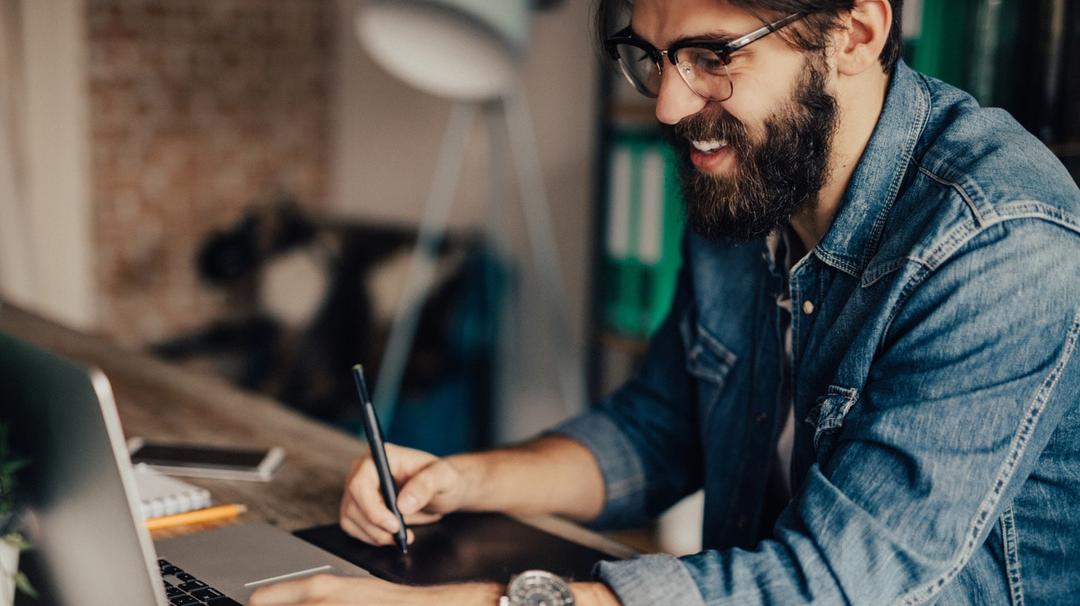 Man sitting at his computer while write on a notepad.